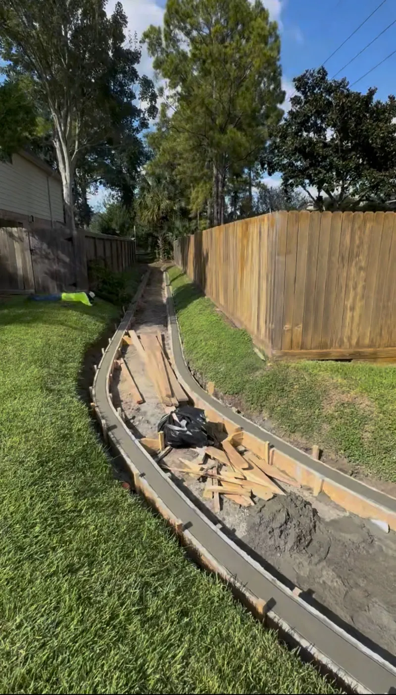 Freshly poured concrete curbs lining a drainage channel between two wood fences