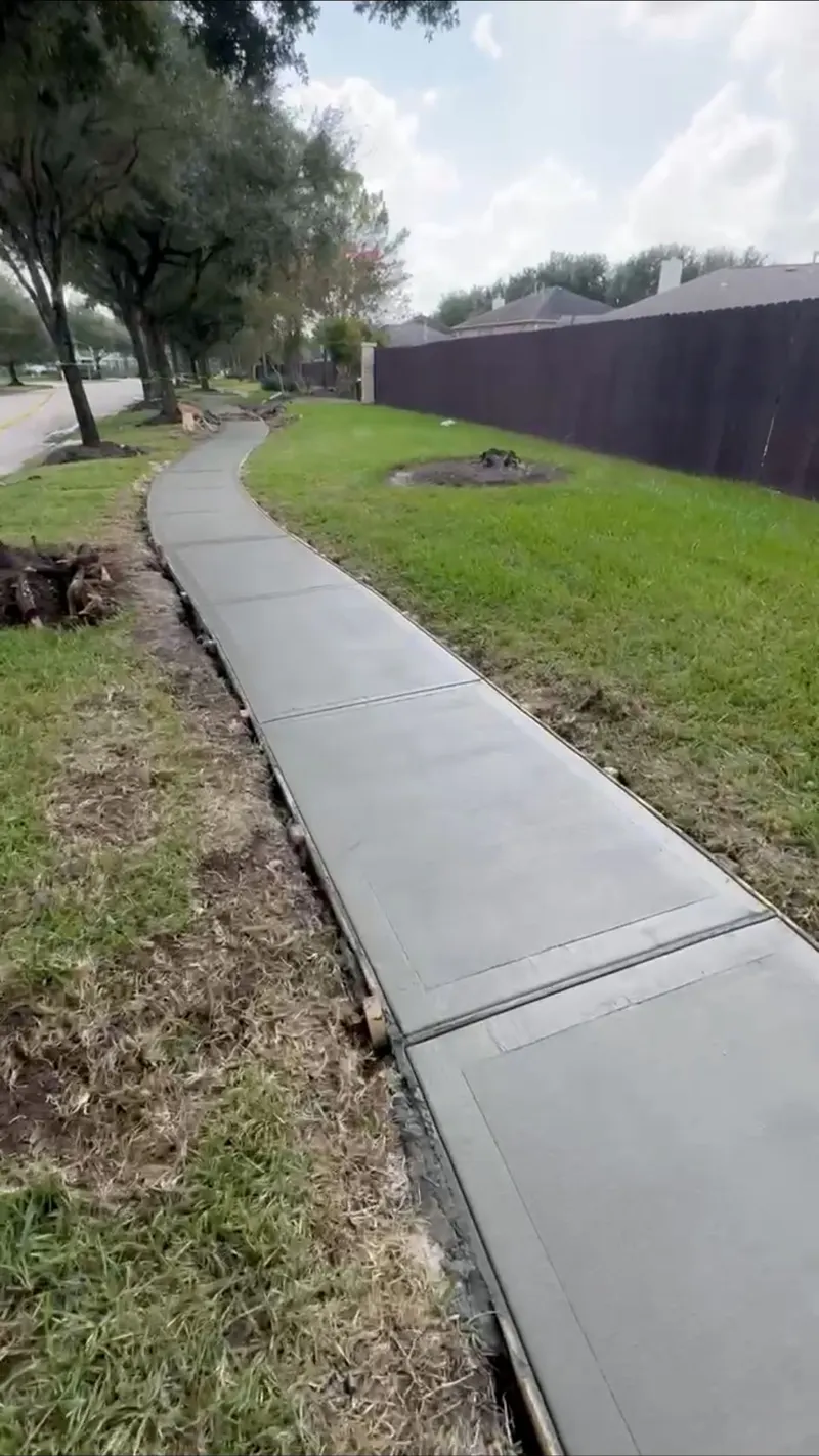Long new concrete sidewalk running along a fence line and lawn