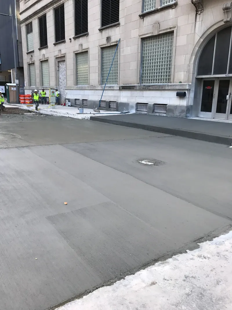 Crew in safety vests beside a freshly poured concrete street in front of a stone office building