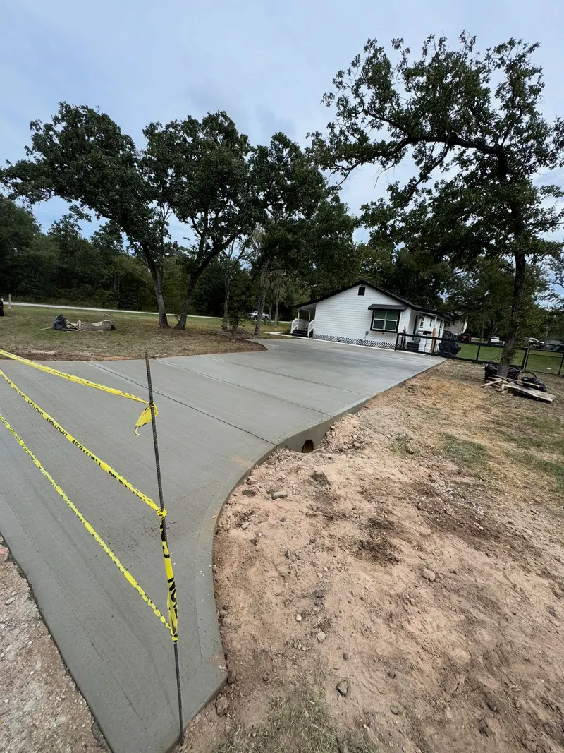 Wide new driveway apron taped off with caution tape, white house and oak trees behind it