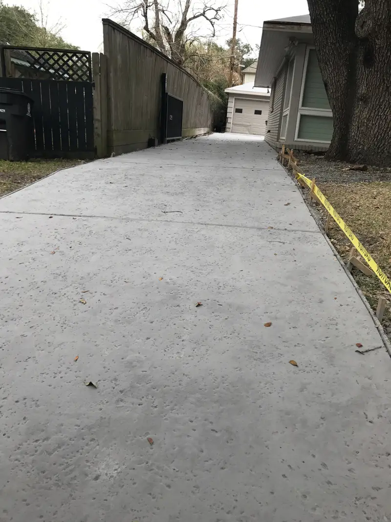 New concrete walkway running along a wood fence beside a house